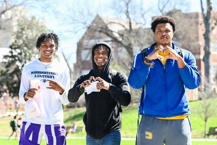 Three male students holding up the Power C and heart hand gestures.